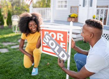 Young couple adding a sold sticker to the for sale sign in front of a house