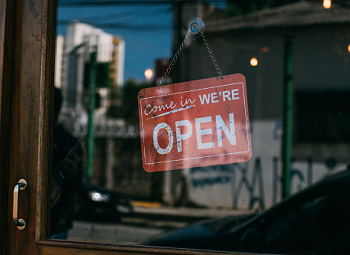 Red come in we're open sign on the front window of a small business